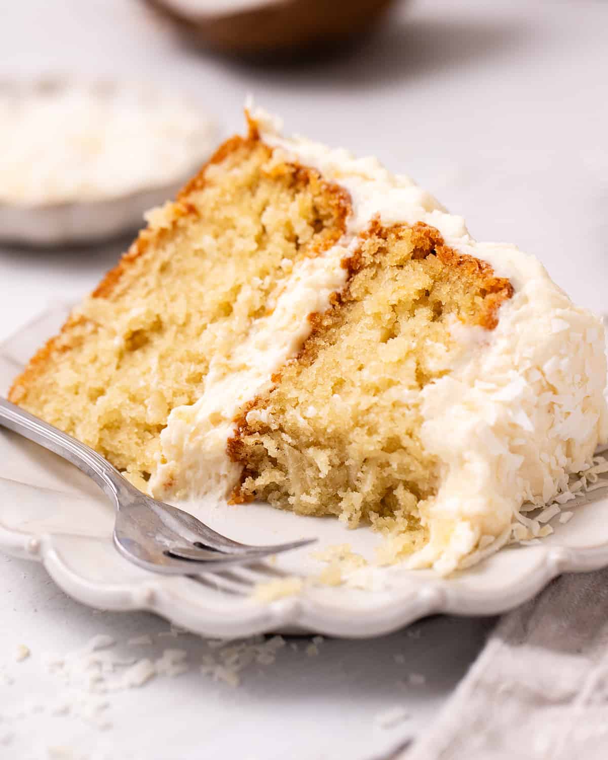 a slice of Coconut Cake on a plate with a fork and a bite taken out of it