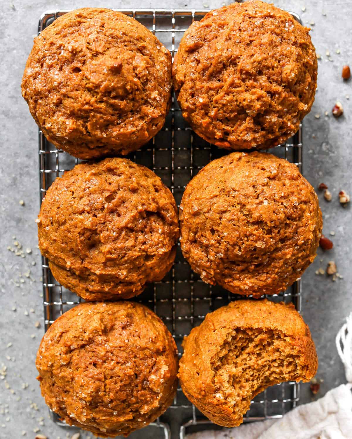 6 Healthy Pumpkin Muffins on a wire cooling rack, one has a bite taken out of it