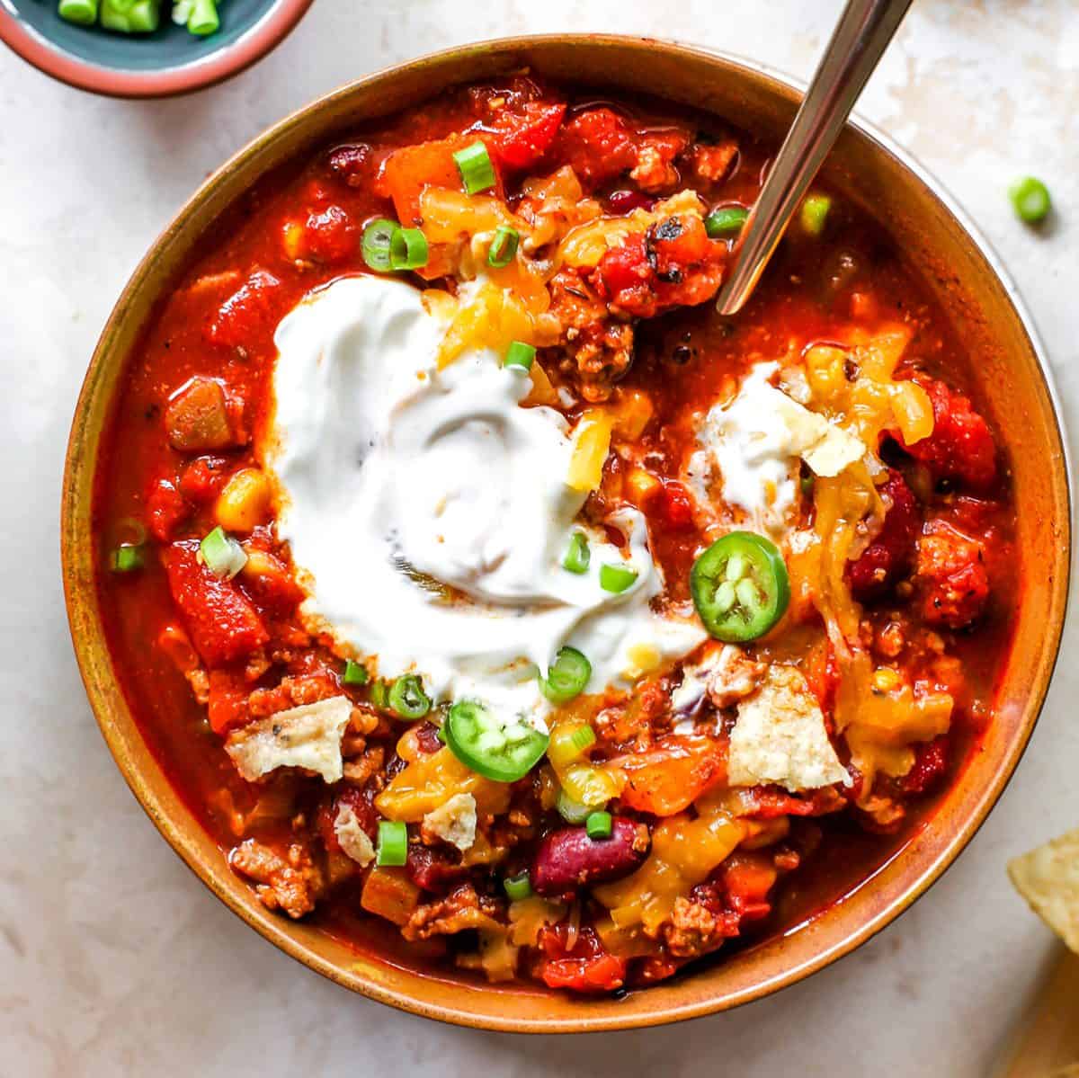 Overhead photo of a bowl of turkey chili with sour cream, cheese and green onions