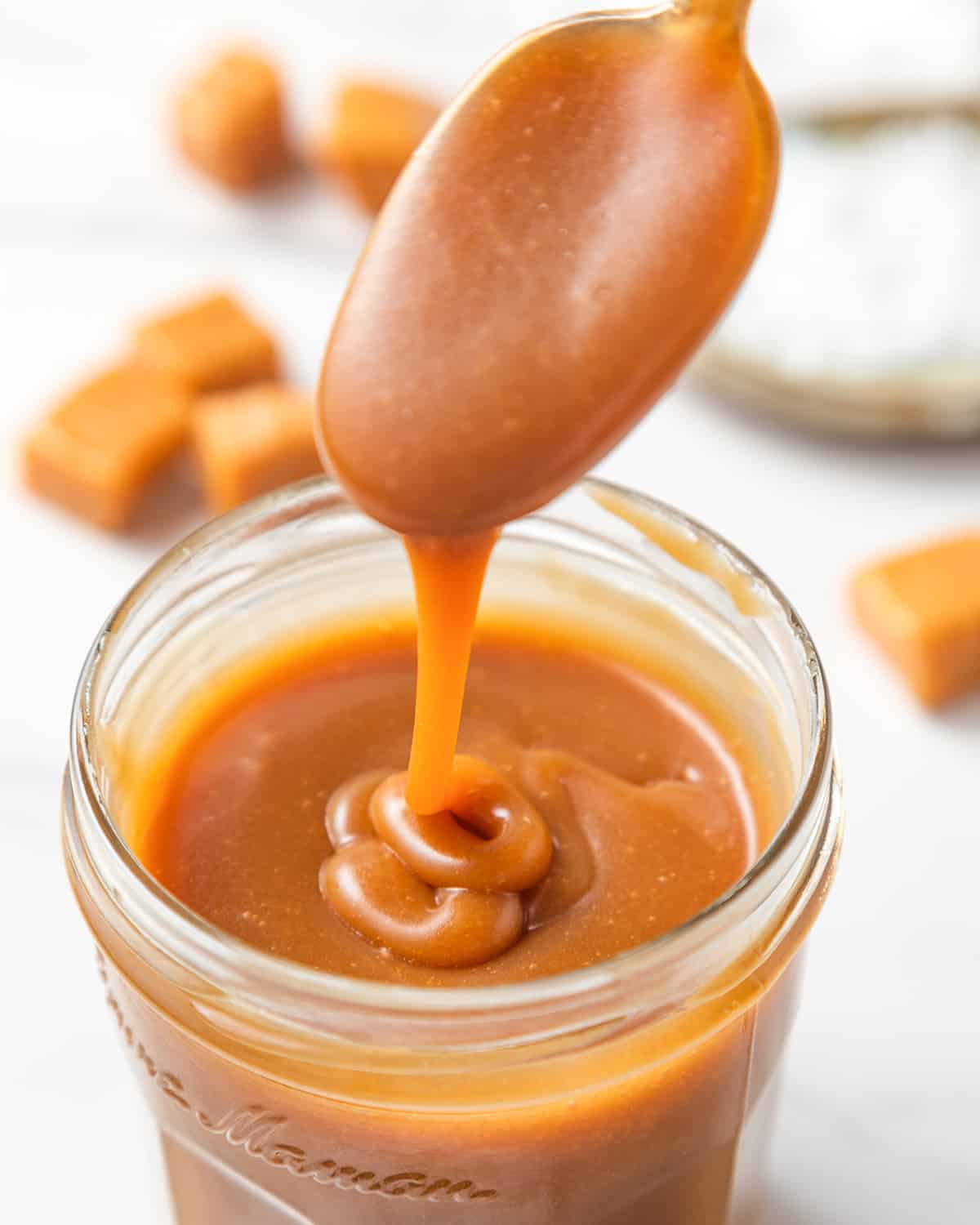 a spoon drizzling caramel sauce into a jar of homemade caramel sauce