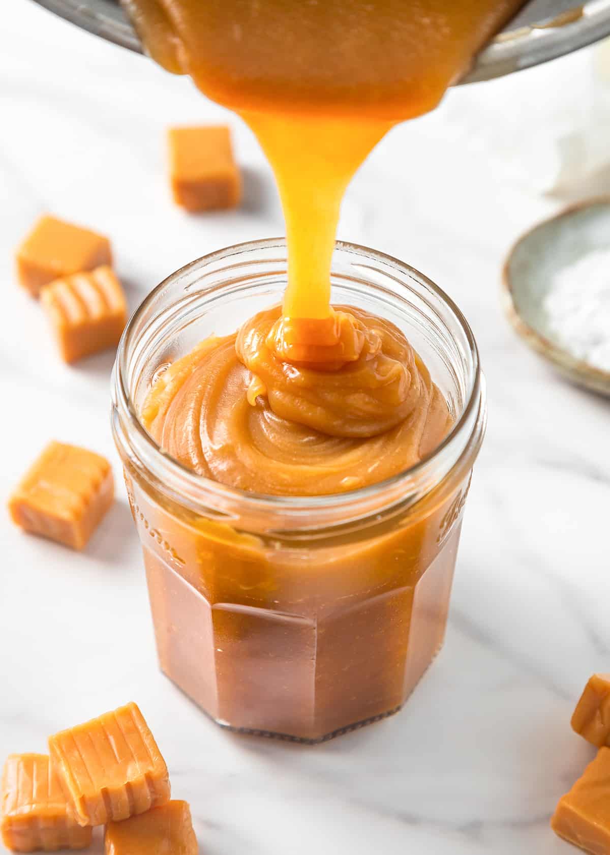caramel sauce being poured from the pan into a glass jar 