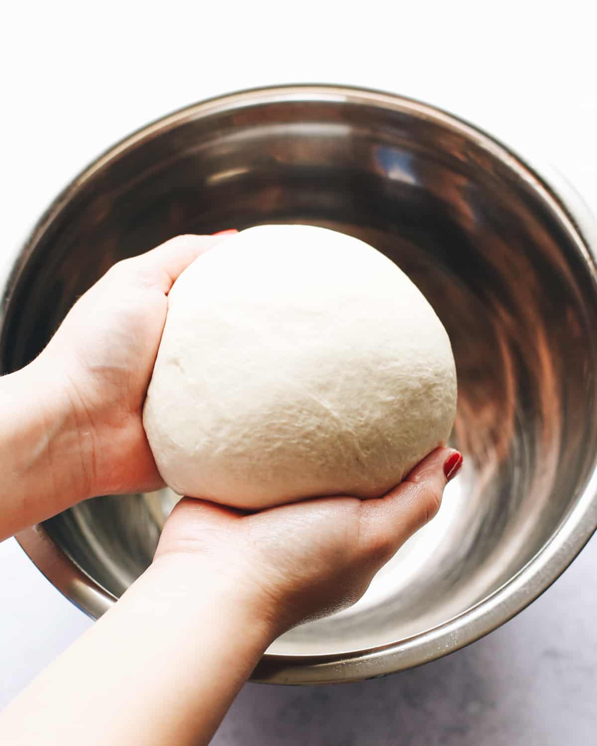 How to Make French Bread - hands holding dough over a bowl