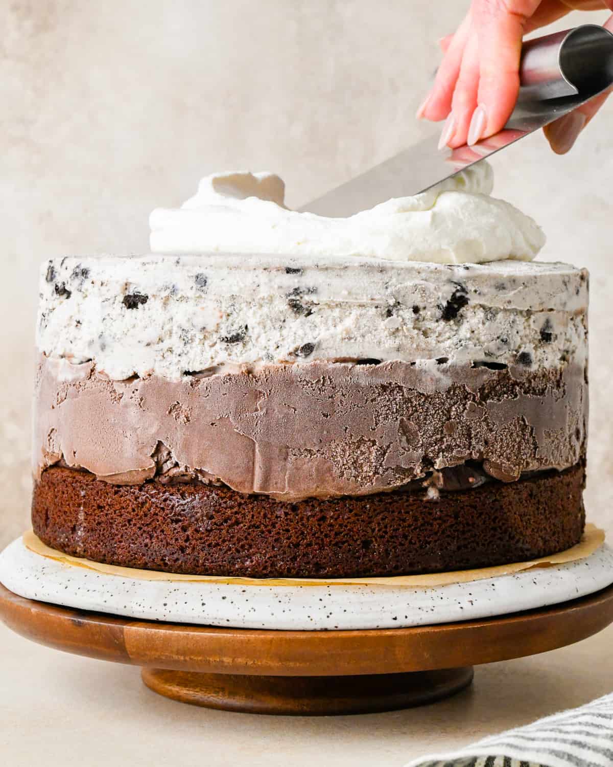 whipped cream being spread over an ice cream cake as frosting