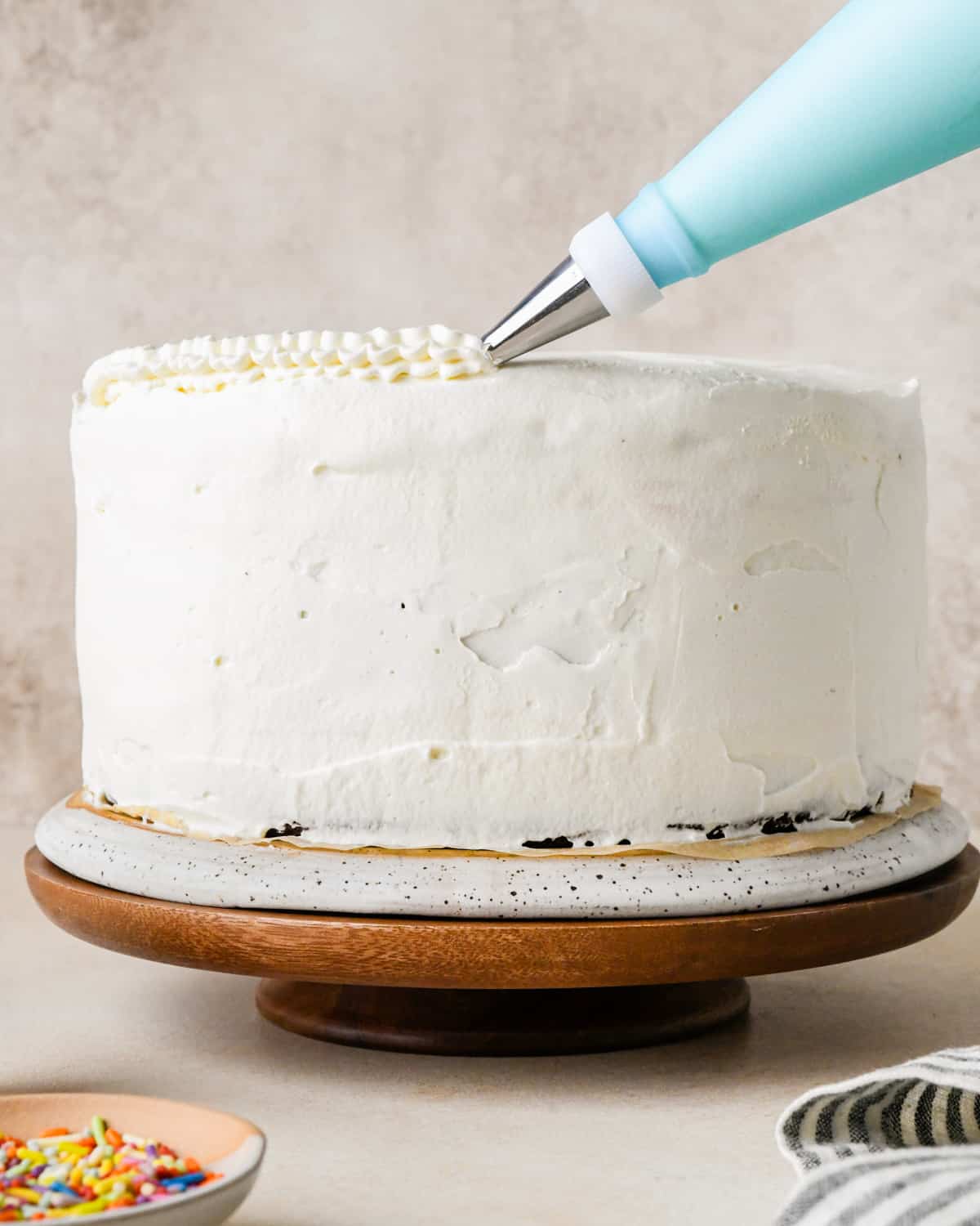 whipped cream being piped onto a frosted ice cream cake