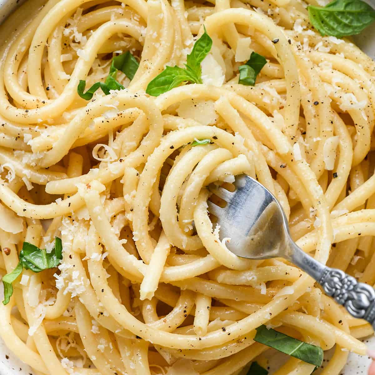 a fork taking a twirl of Parmesan Pasta in a bowl topped with fresh basil, parmesan cheese and pepper. 