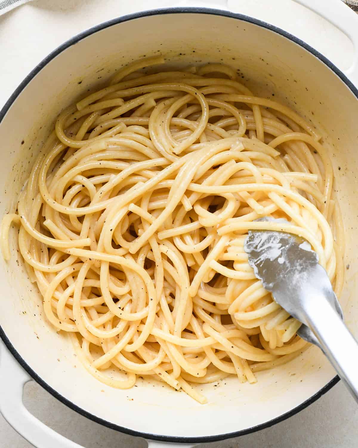 How to Make Parmesan Pasta - tongs stirring pasta into the cheese sauce