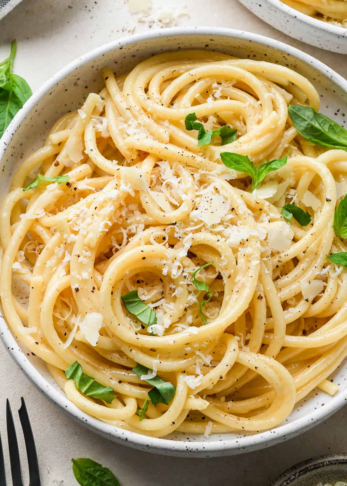 Parmesan Pasta on a plate with a fork garnished with parmesan cheese and fresh basil