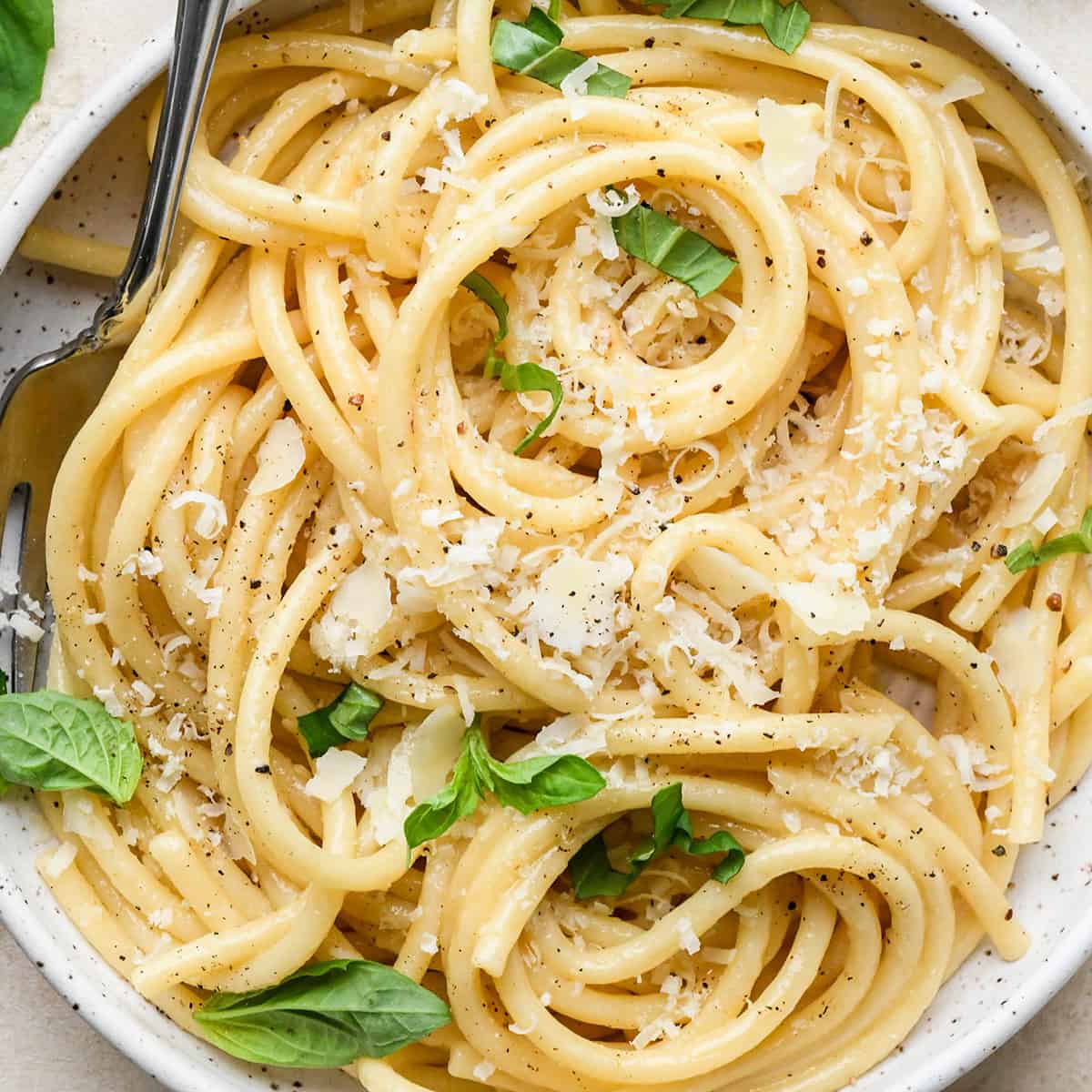 Parmesan Pasta on a plate with a fork garnished with parmesan cheese and fresh basil