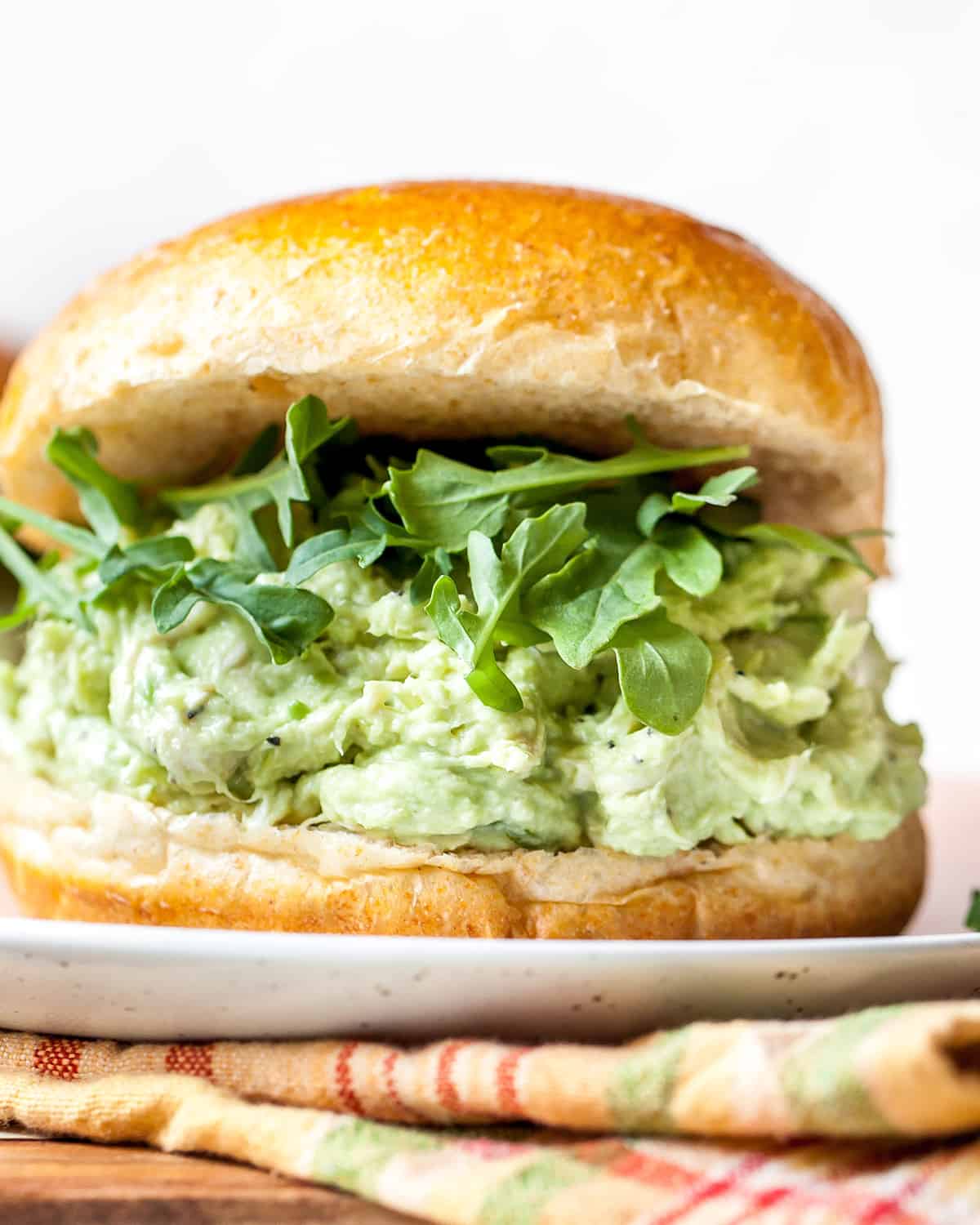 up close photo of an avocado chicken salad sandwich on a bun with arugula