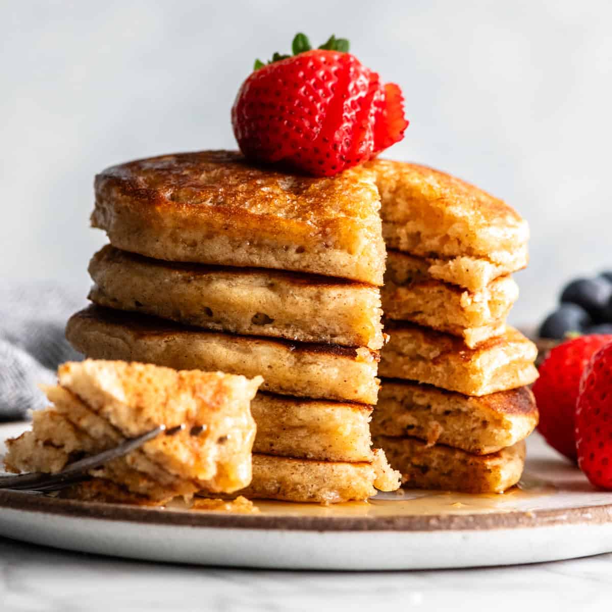a stack of 5 whole wheat pancakes with a bite cut out of them on a fork next to the stack on a plate