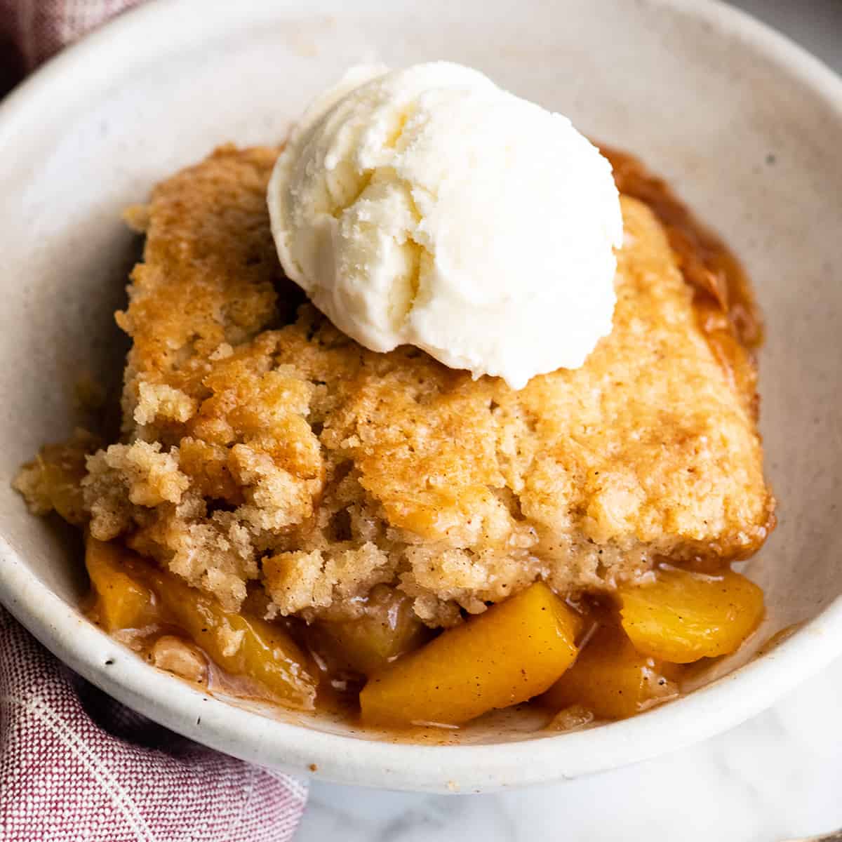 peach cobbler in a bowl topped with vanilla ice cream