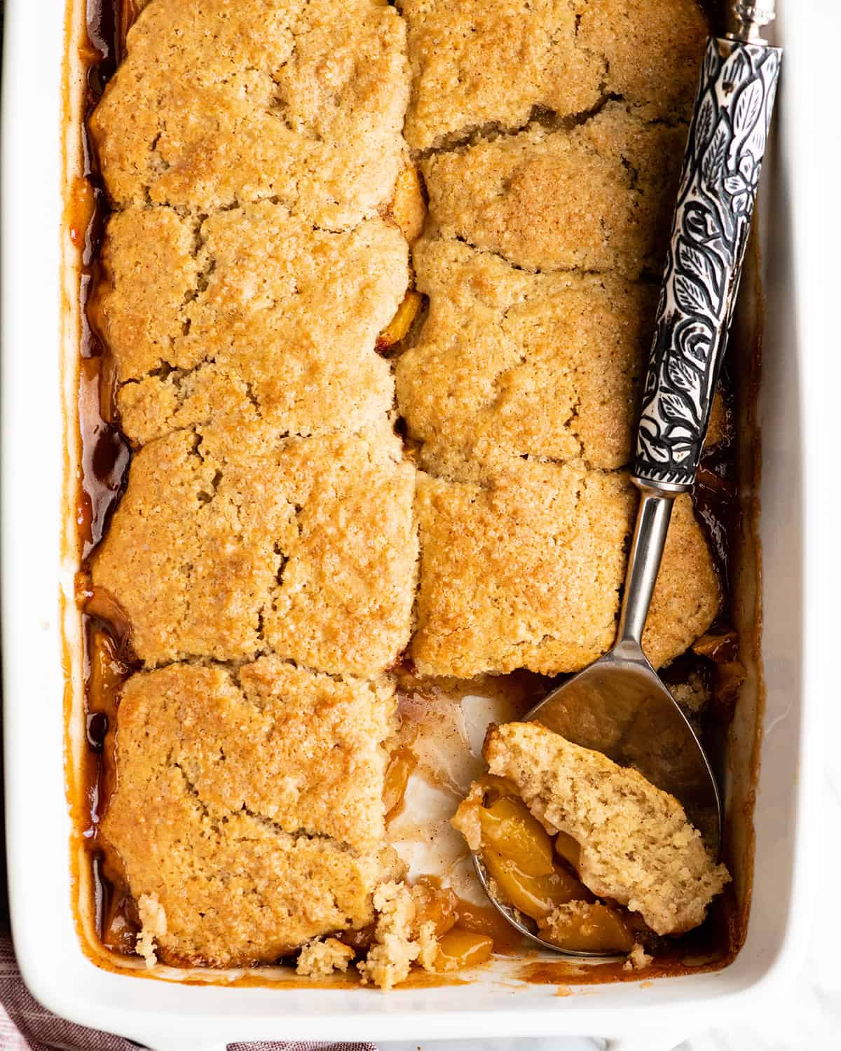 peach cobbler in a baking dish with a serving spoon