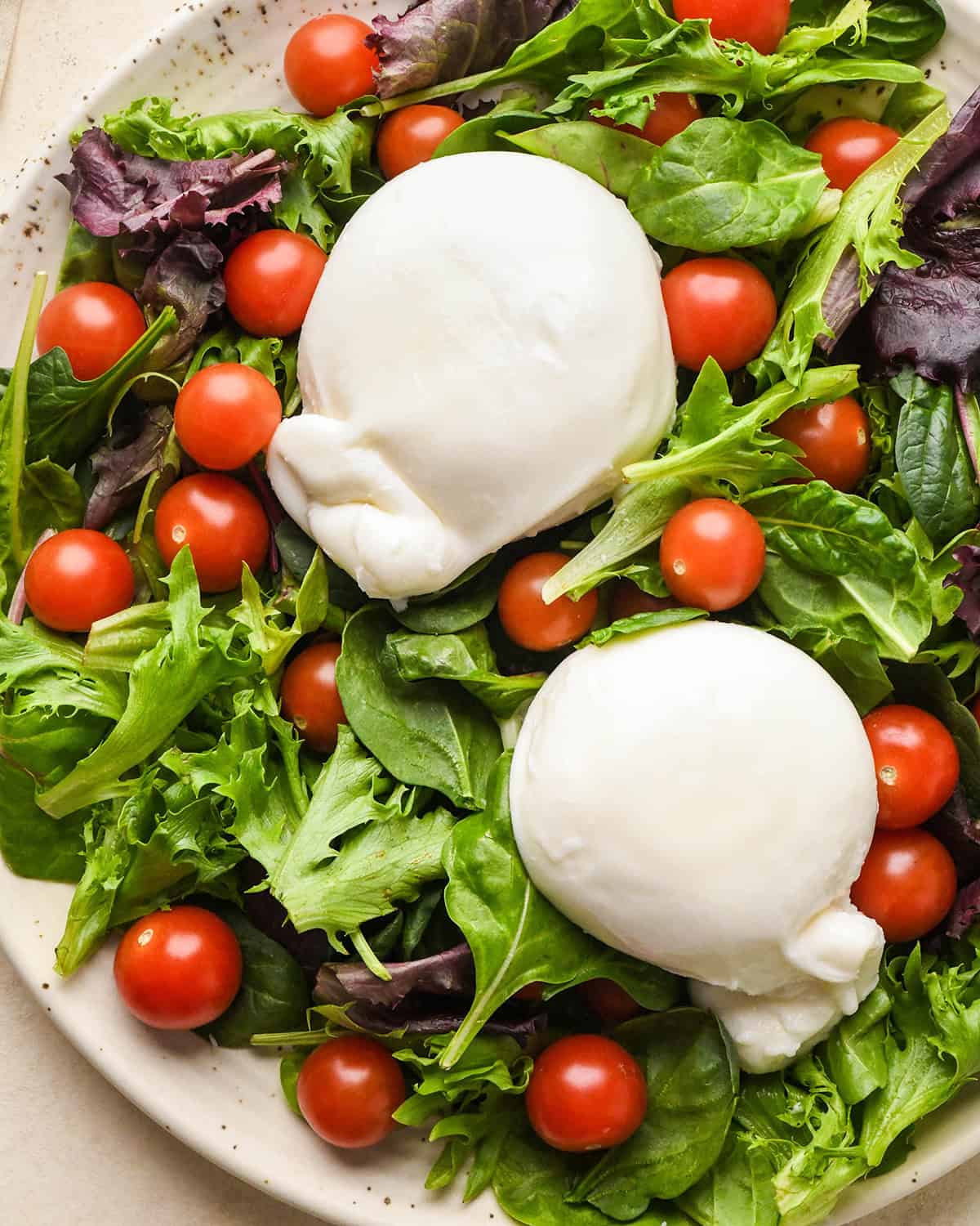 how to assemble burrata salad - tomatoes, spring mix and burrata cheese on a plate