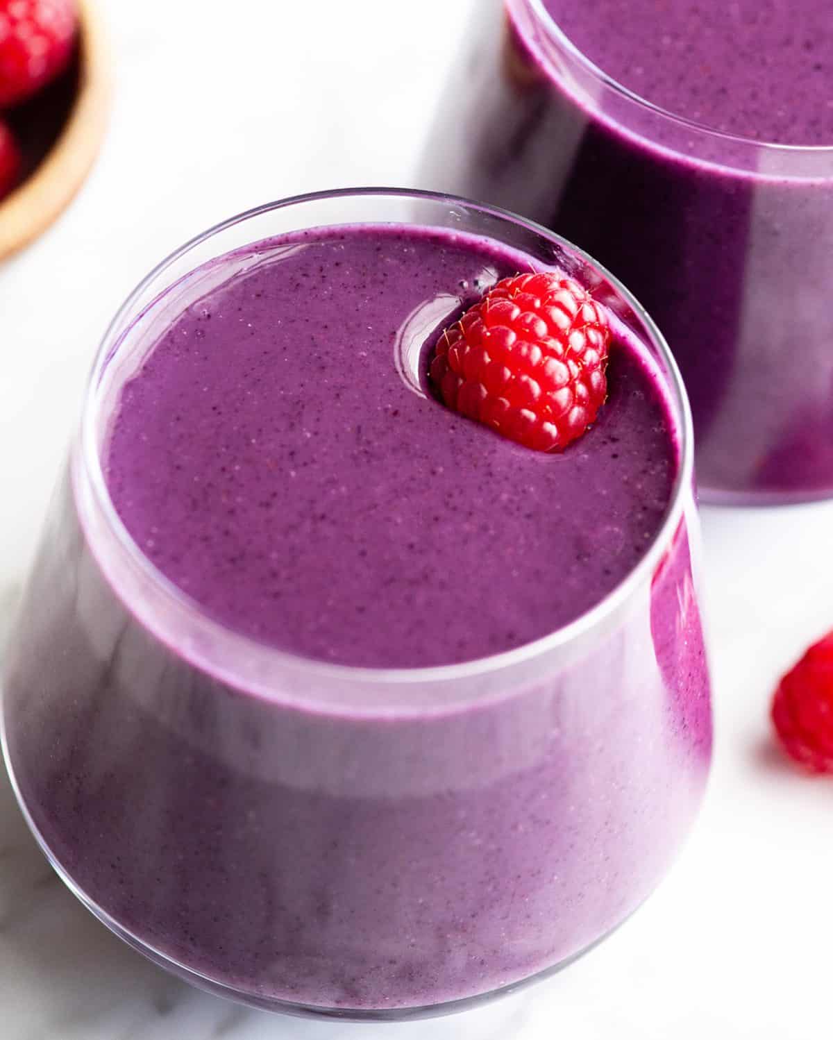 up close photo of a mixed berry smoothie in a glass with a raspberry on top