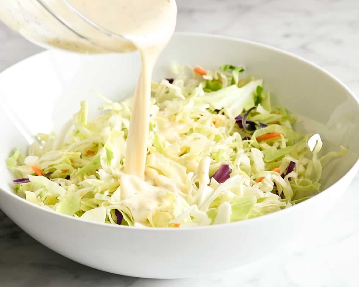 How to Make Coleslaw - pouring dressing over cabbage mixture in a bowl