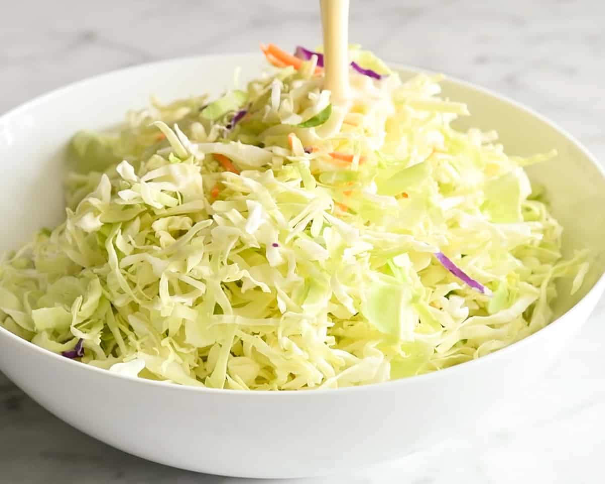 How to Make Coleslaw - pouring dressing over the rest of the coleslaw in a bowl