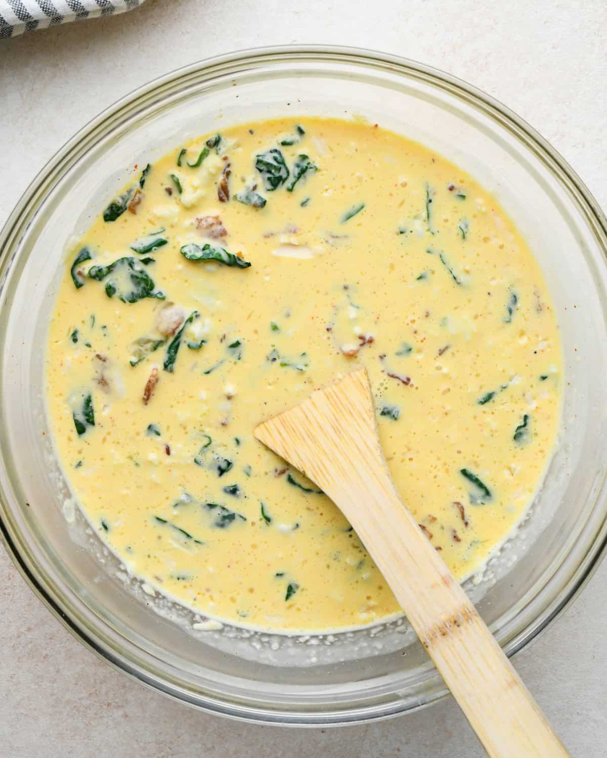 bacon spinach quiche filling in a bowl with a wooden spoon