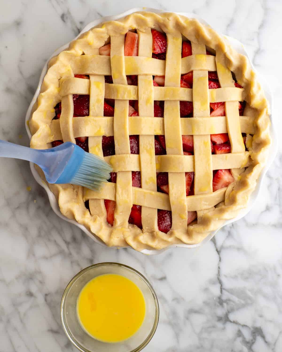 egg wash being brushed on the lattice crust of a strawberry pie