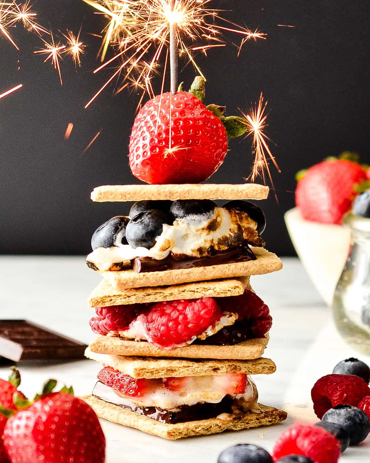 a stack of 3 Berry S'mores with a strawberry and a lit sparkler on top