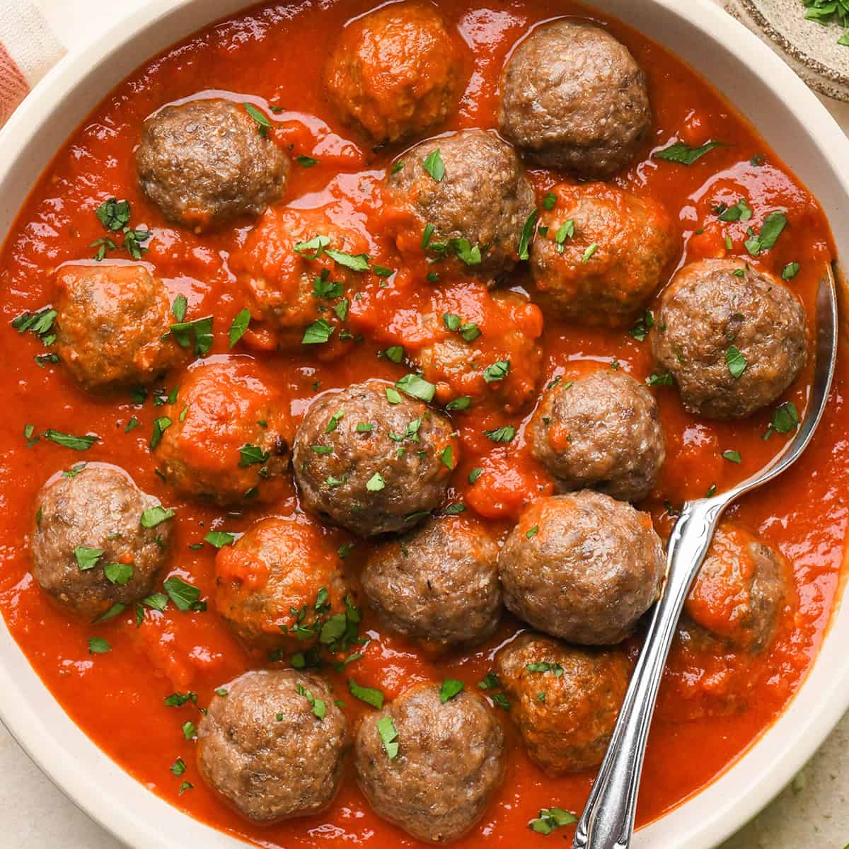 Gluten Free Meatballs garnished with basil in a bowl in marinara sauce with a spoon. 