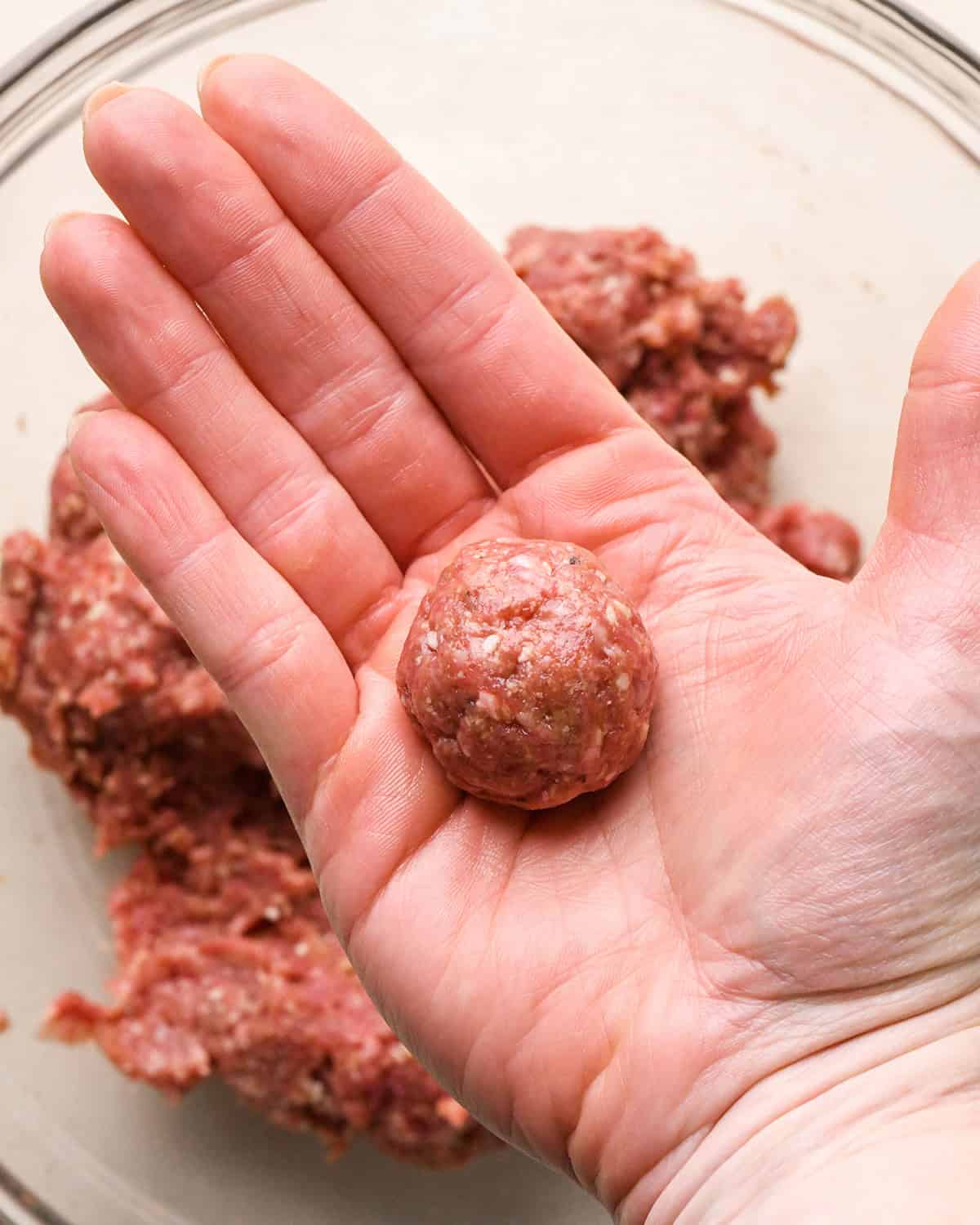 a hand rolling a gluten free meatball into a ball