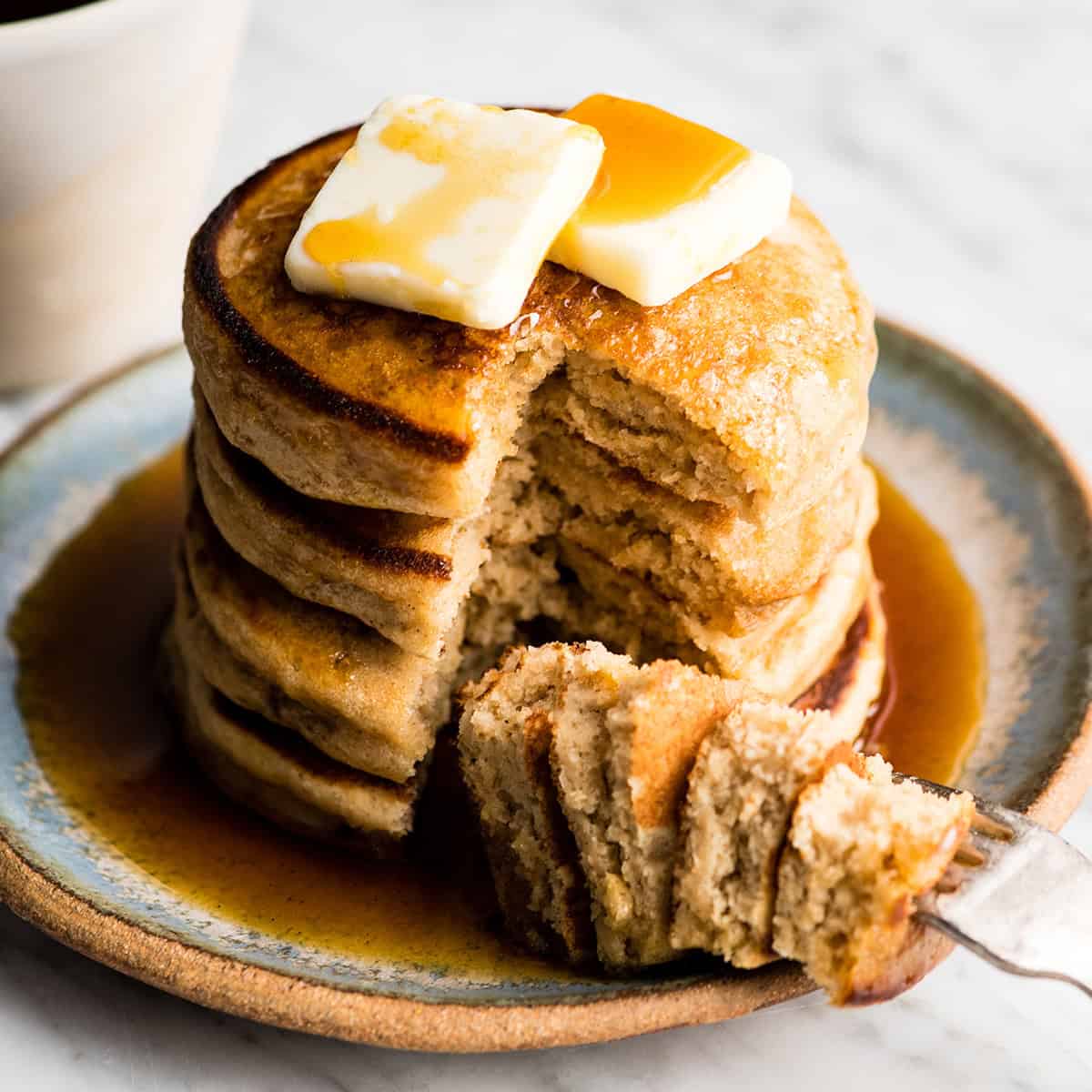 a stack of 4 Greek Yogurt Pancakes with butter and syrup. A bite is cut out of the stack on a fork on the plate. 