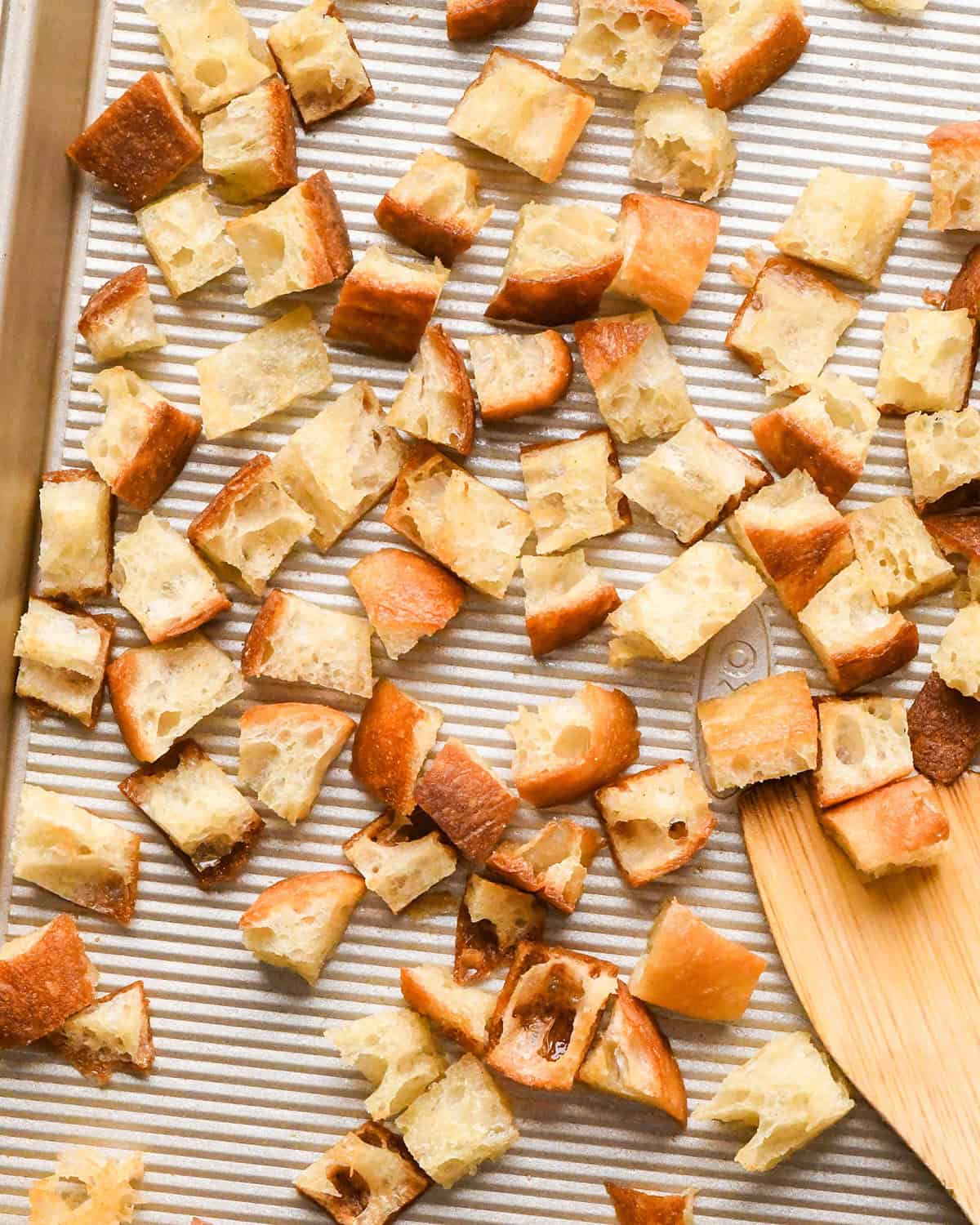 Homemade Croutons on a baking sheet with a wooden spatula