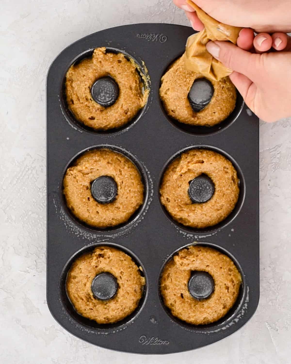 Baked Pumpkin Donuts batter being piped into the wells of a donut pan