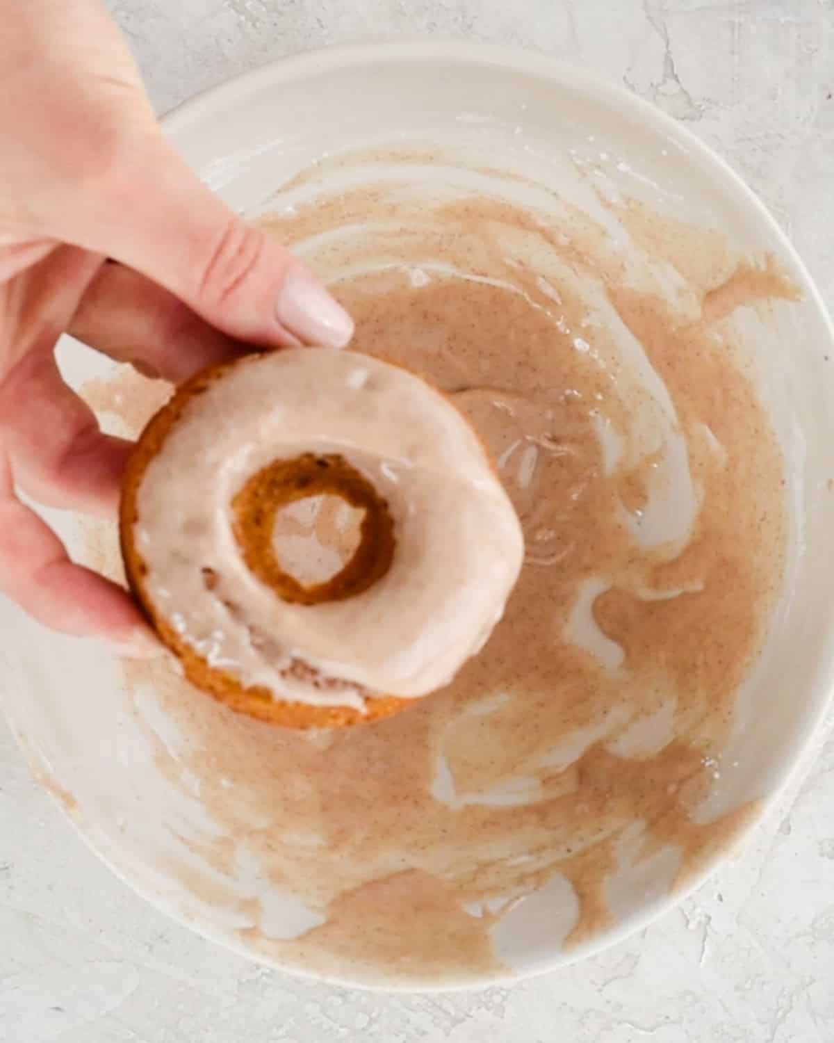 a baked pumpkin donut being dipped in glaze 