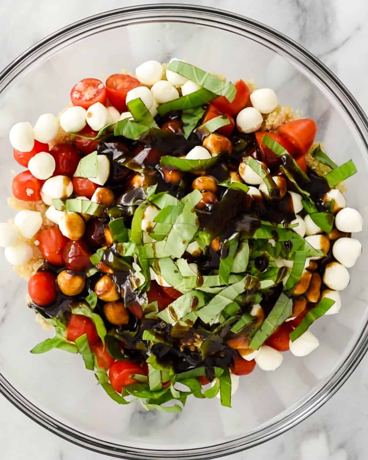 assembling Caprese Quinoa Salad in a large glass bowl - before stirring
