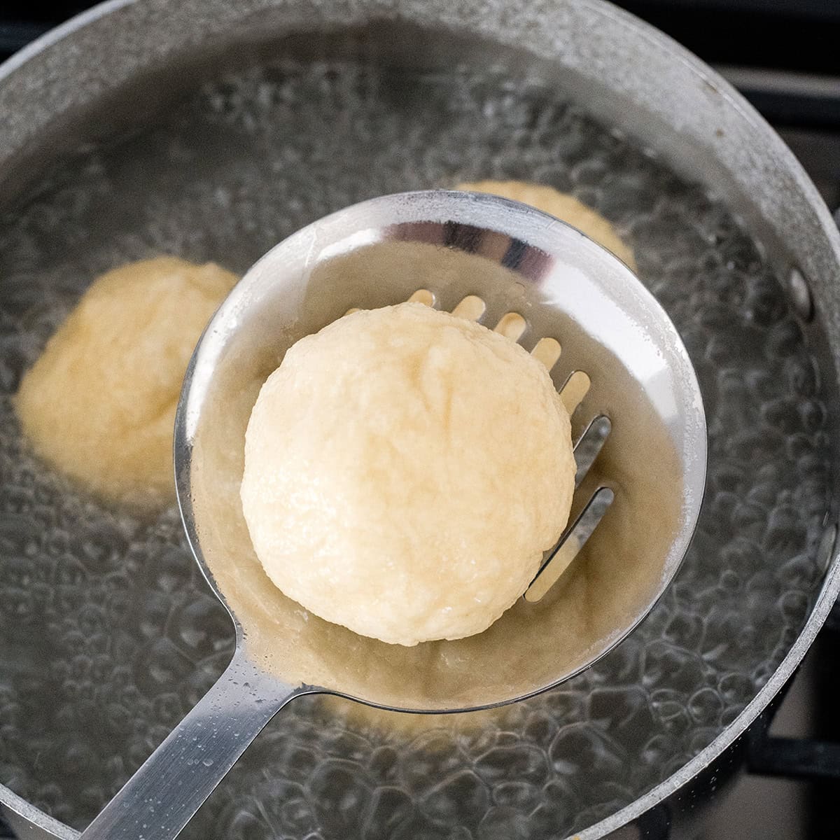 Cheese Pretzel Bites boiling in a baking soda bath, one being lifted out with a slotted spoon