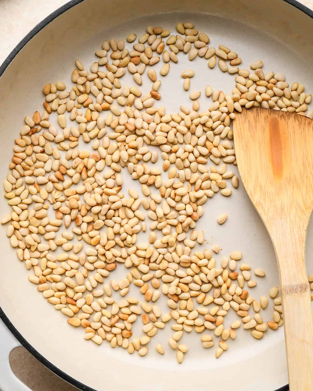 How to Make Chicken Curry - toasted pine nuts in a pan with a wooden spatula