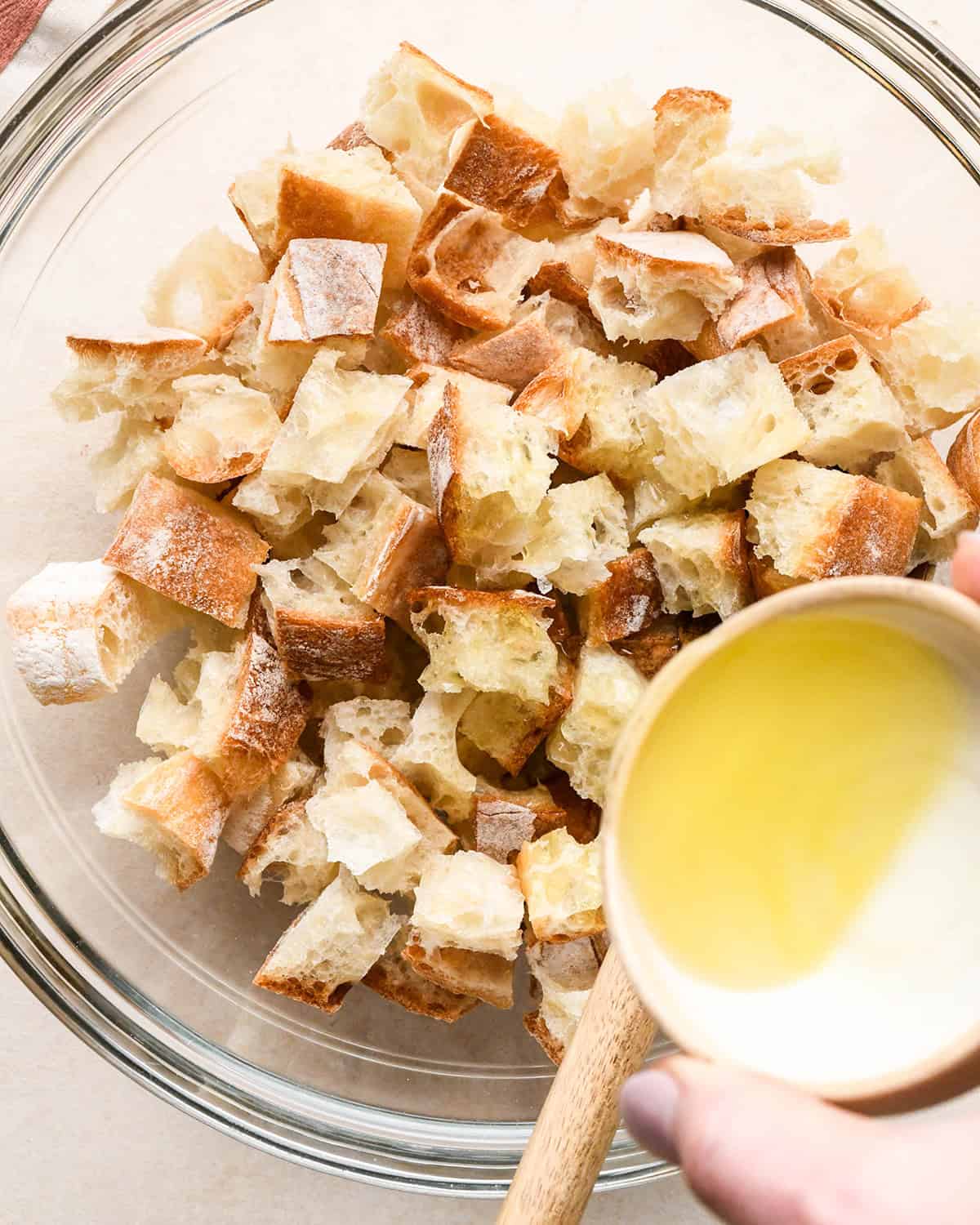 How to Make Croutons - pouring olive oil over bread cubes in a bowl