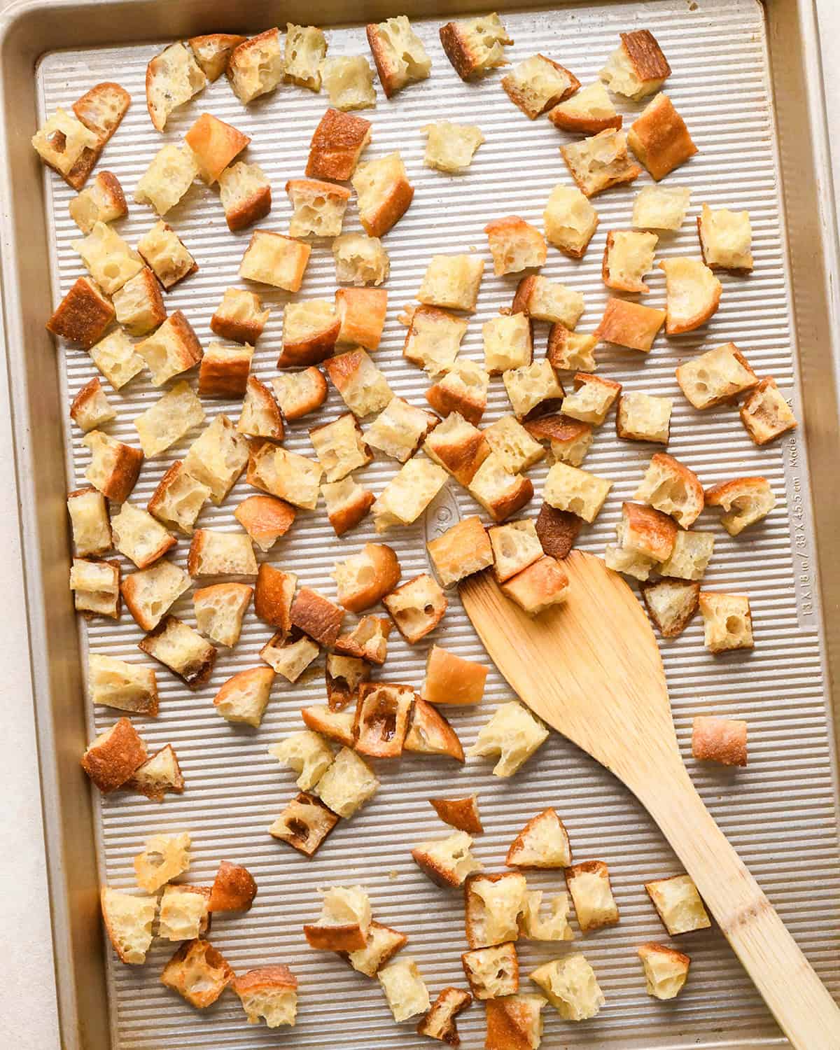 How to Make Croutons - stirring baked croutons on a baking sheet with a wooden spatula
