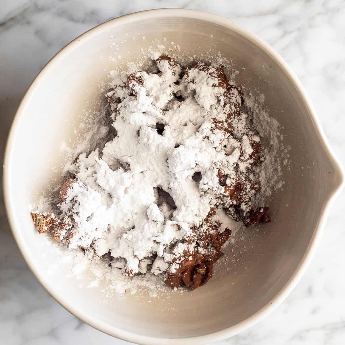 How to Make Puppy Chow - adding powdered sugar to the chocolate coated cereal