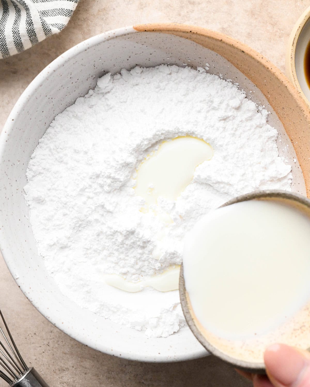 How to Make Vanilla Icing - milk being poured  over powdered sugar in a bowl