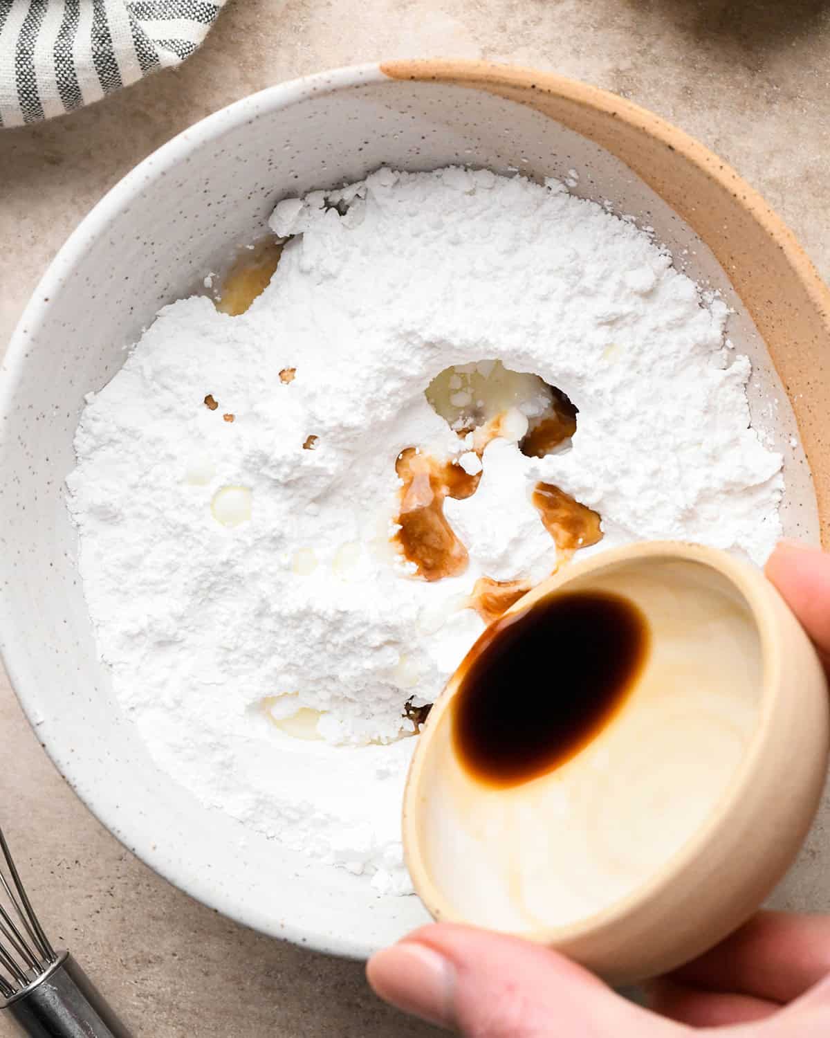 How to Make Vanilla Icing vanilla being poured over powdered sugar in a bowl