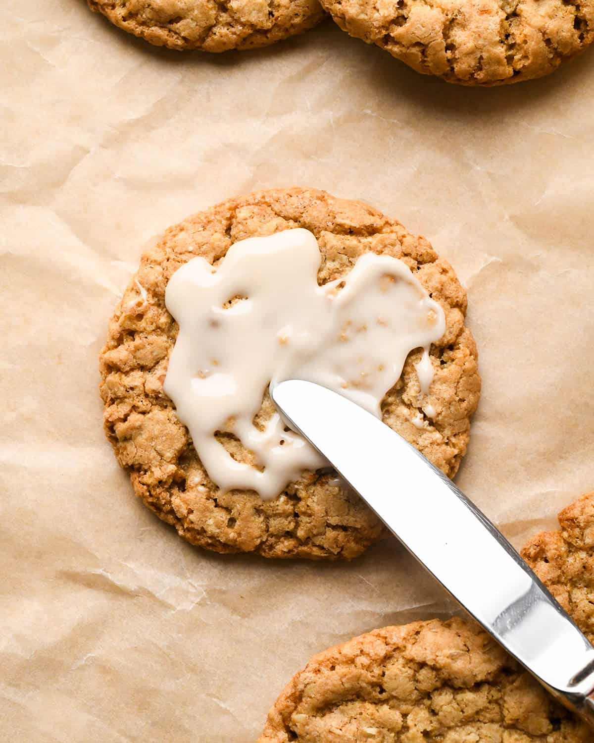 vanilla icing being spread on Iced Oatmeal Cookies