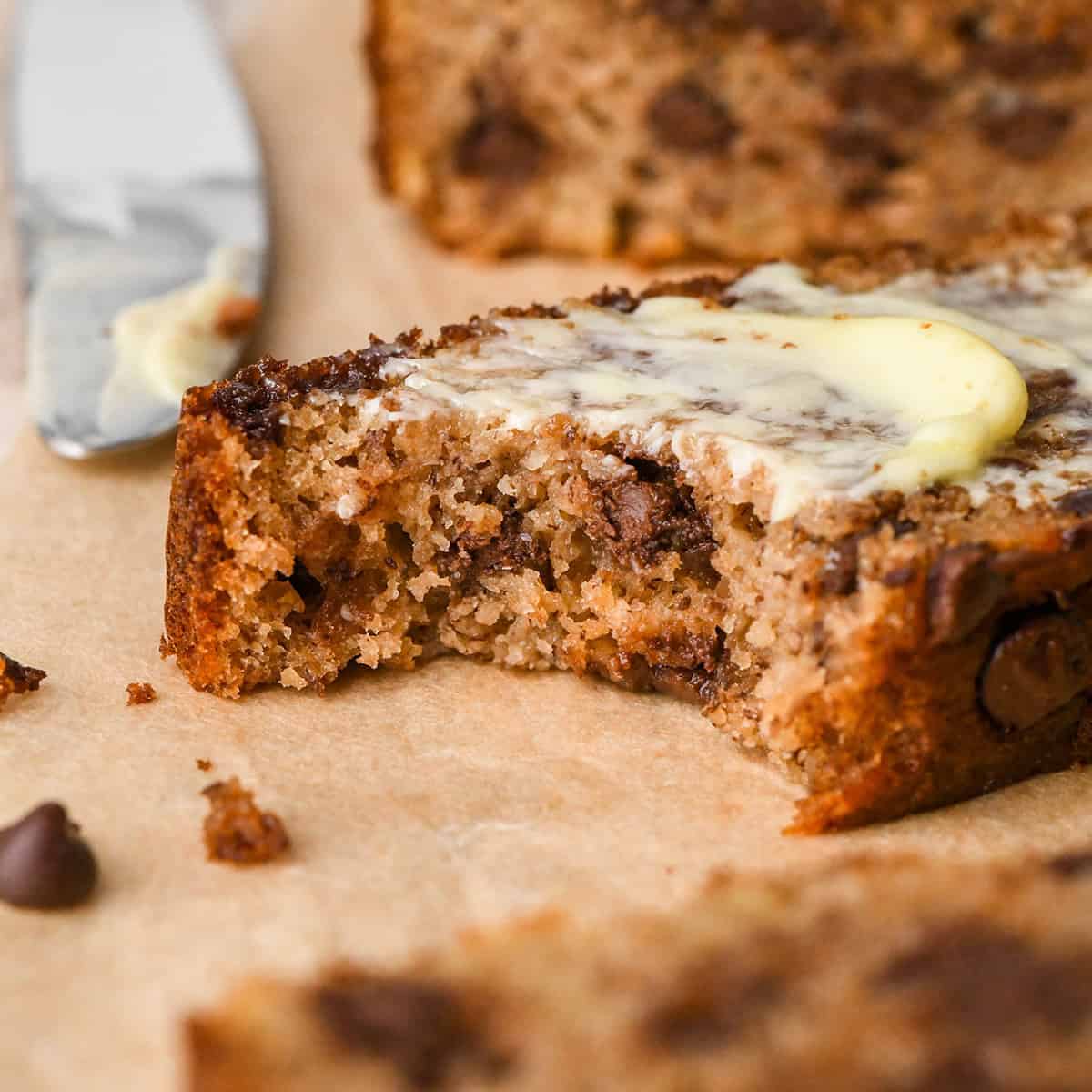 front view of a slice of Paleo Banana Bread with butter on top and a bite taken out of it