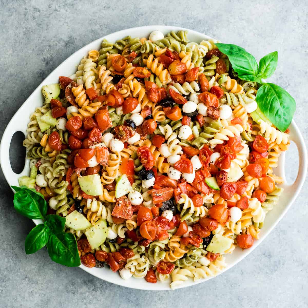 overhead photo of best pasta salad recipe in a white serving dish garnished with basil