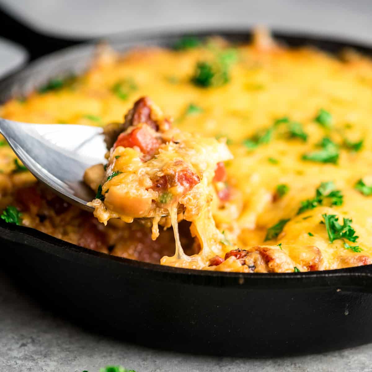 a spoon taking a scoop of quinoa casserole out of a cast iron skillet