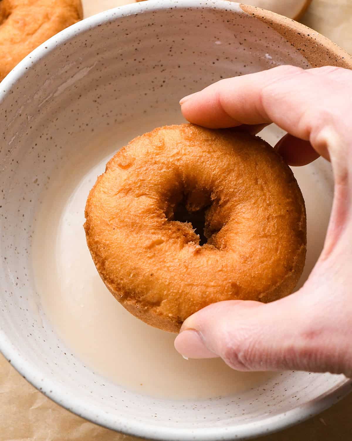 a donut being dipped into vanilla glaze