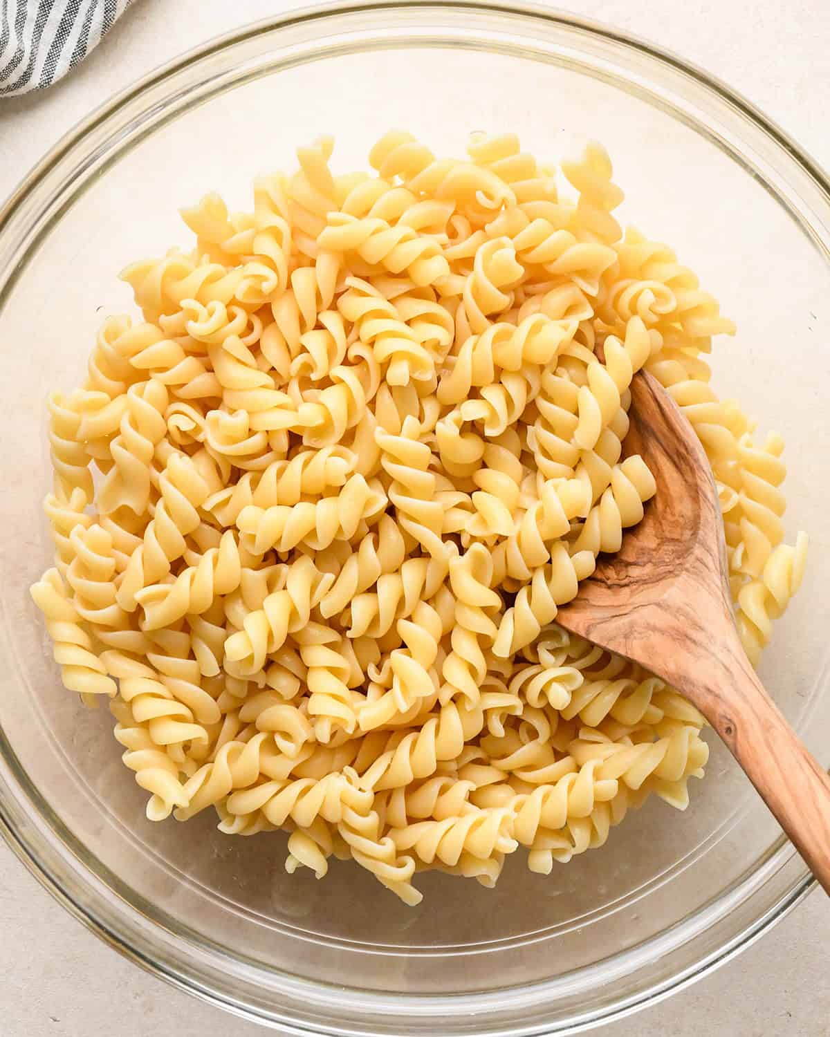 rotini pasta in a glass bowl with a wooden spoon