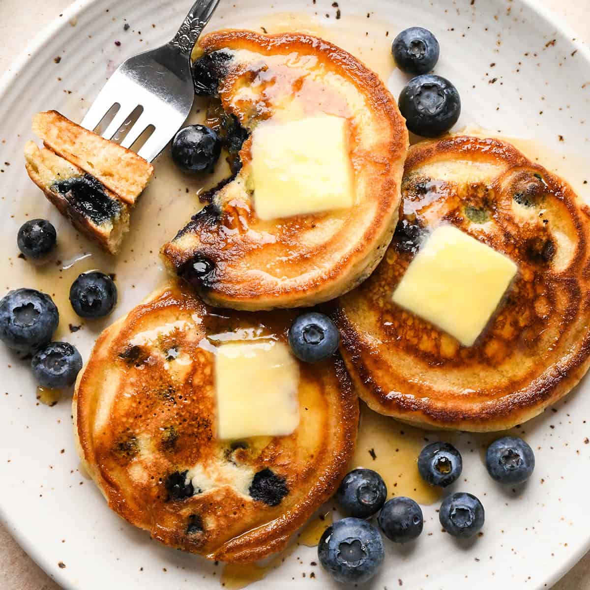 3 Blueberry Pancakes on a plate plus a fork with a bite on it