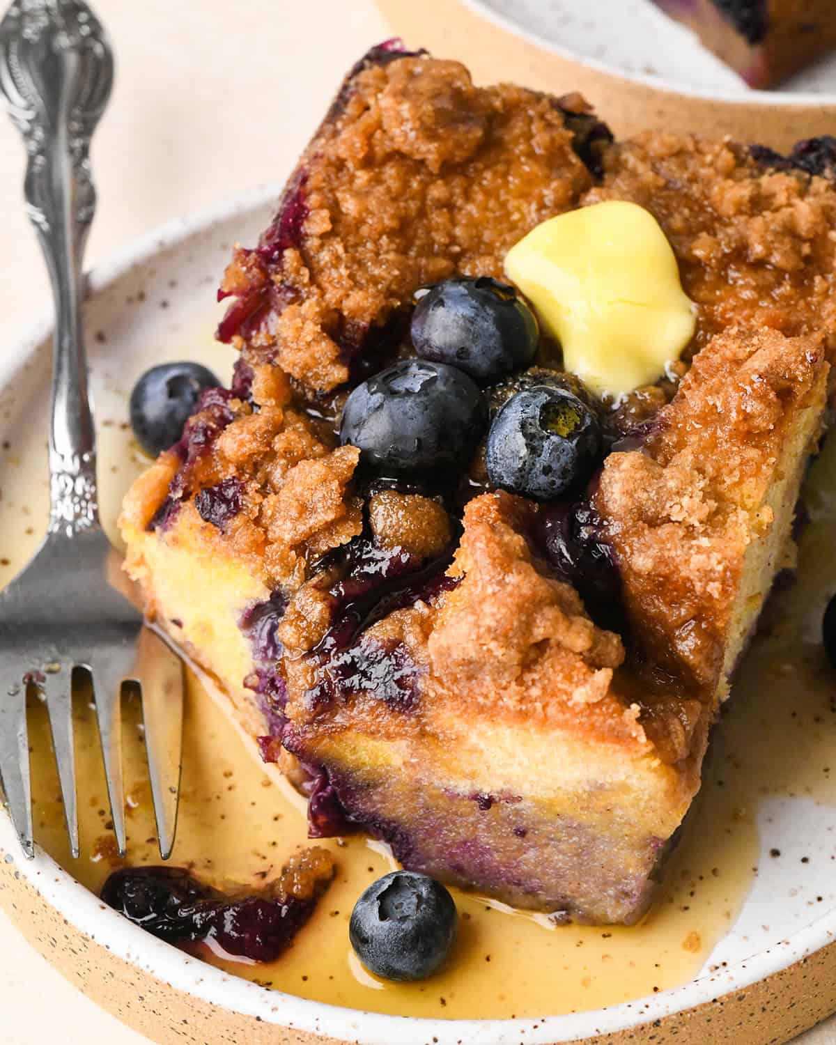 a piece of Blueberry French Toast Casserole  on a plate with butter, blueberries and syrup. 