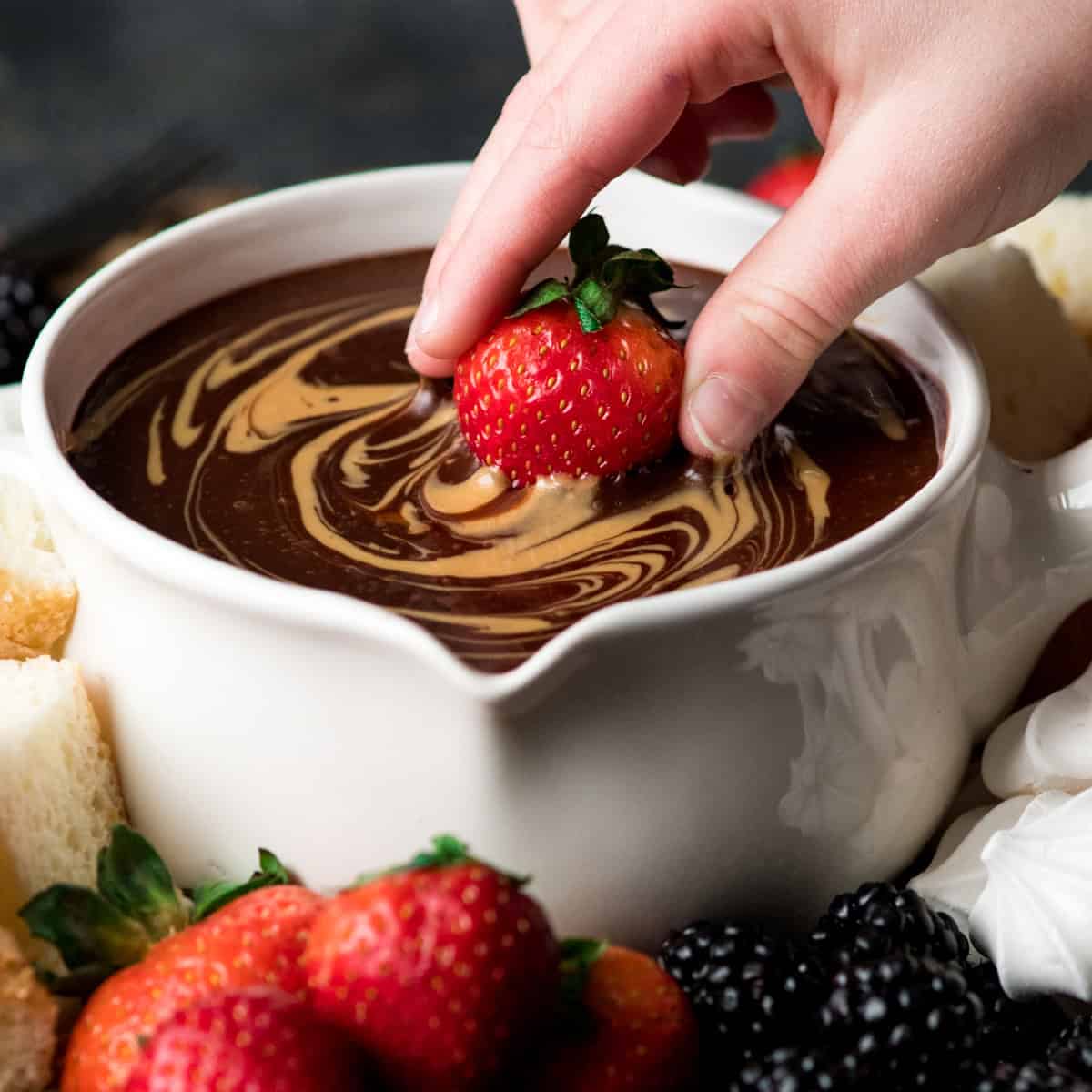 a strawberry being dipped into  Chocolate Peanut Butter Fondue in a white fondue pot