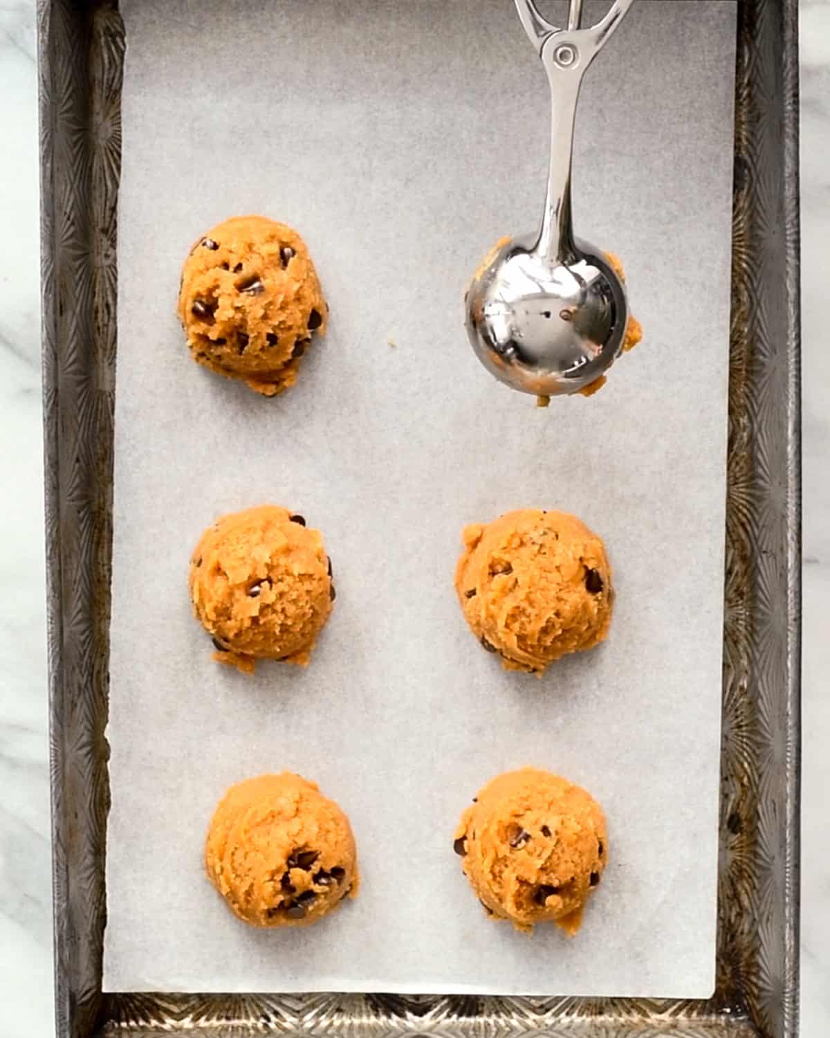 a cookie scoop measuring dough onto a baking sheet