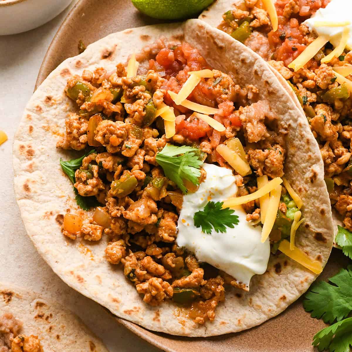 two Ground Turkey Tacos on a plate with sour cream, cilantro, salsa and cheese