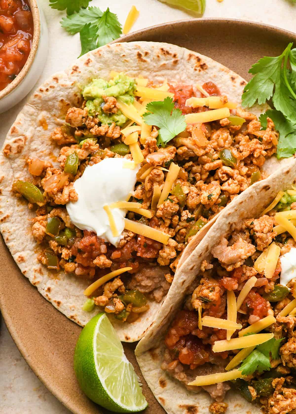 two Ground Turkey Tacos on a plate with sour cream, cilantro, salsa and cheese