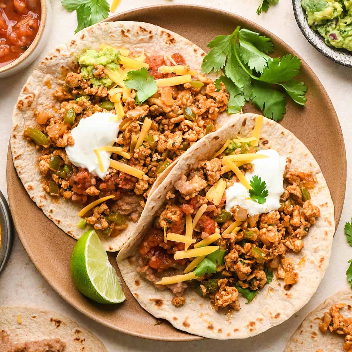 two Ground Turkey Tacos on a plate garnished with sour cream, cilantro, cheese and salsa